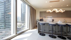 A modern kitchen with a large window, a bar area with stools, and a view of the cityscape. - 3BHK Sea View Near Palm Jumeirah Avani  (Dubai)