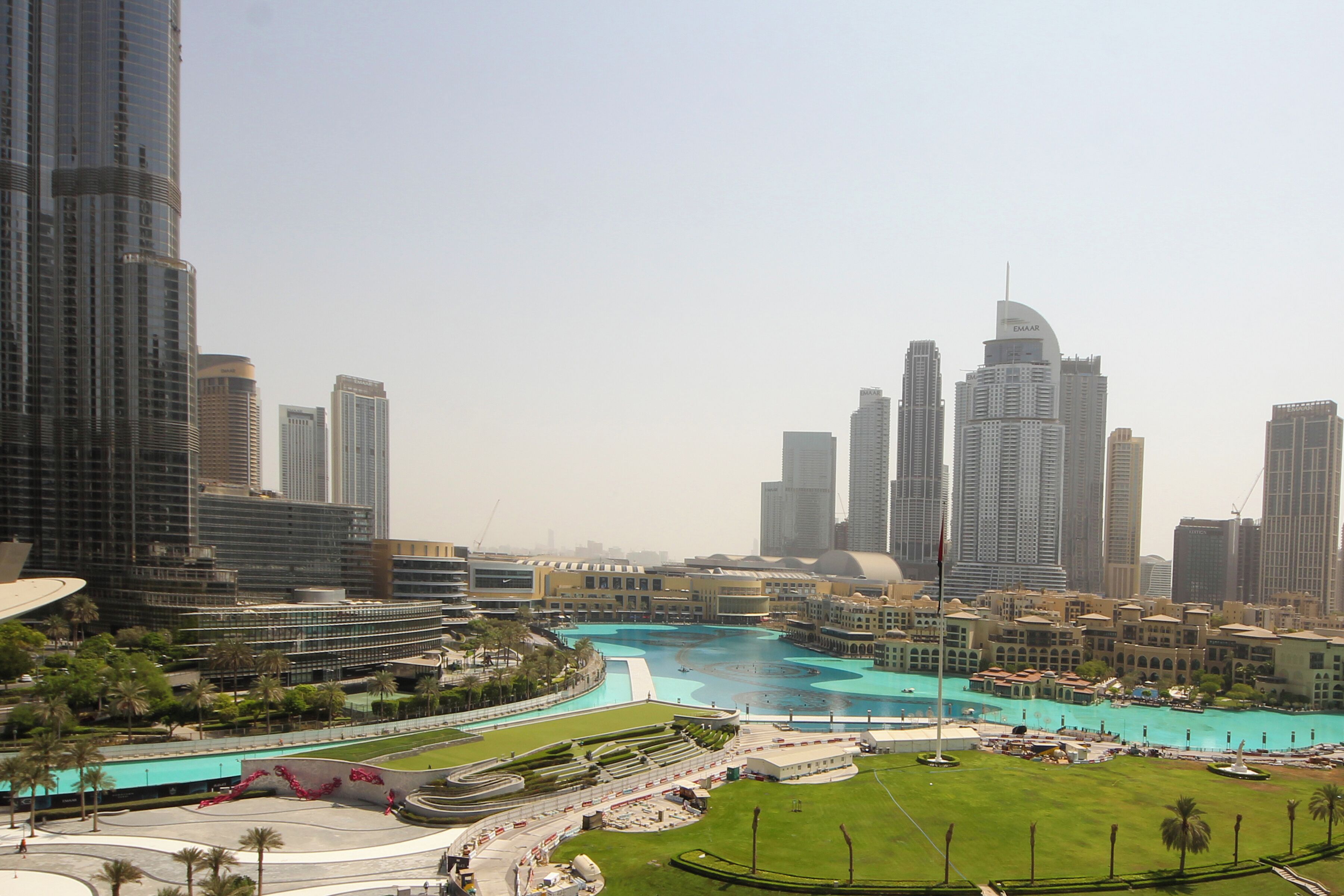 A cityscape with modern high-rise buildings, a central water feature, and a well-maintained park area.