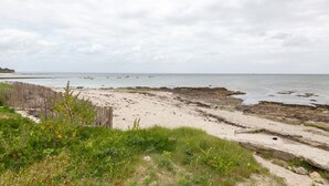 Paisatge costaner amb una platja sorrenca, costa rocosa i una tanca de fusta.