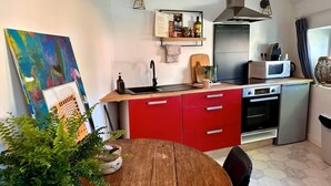 Een kleine keuken met een rode aanrecht, roestvrijstalen apparatuur en een houten eettafel.