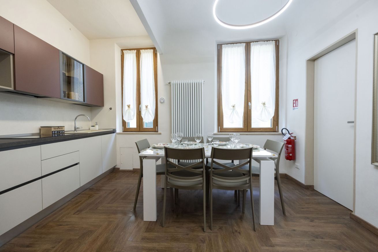 A modern kitchen with a dining area, wooden flooring, and large windows.