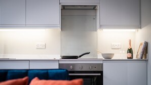 A modern kitchen with white cabinets, a stove, a frying pan, a bowl, and a bottle of champagne. - Dalton Sq Apartments (Lancaster)