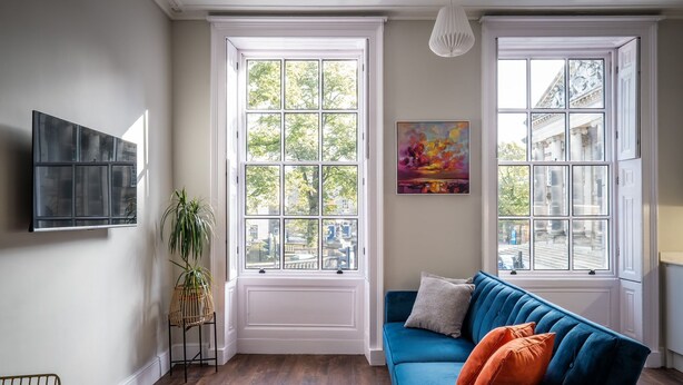 A room with a blue sofa, a potted plant, and a painting on the wall. - Dalton Sq Apartments (Lancaster)