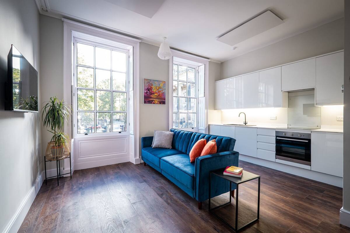 Una sala de estar moderna con un sofá azul, una mesita y una cocina con armarios blancos y una estufa.
