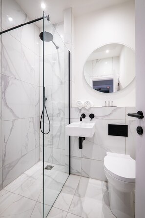 A modern bathroom with a glass-enclosed shower, a white sink, and a toilet. - Dalton Sq Apartments (Lancaster)