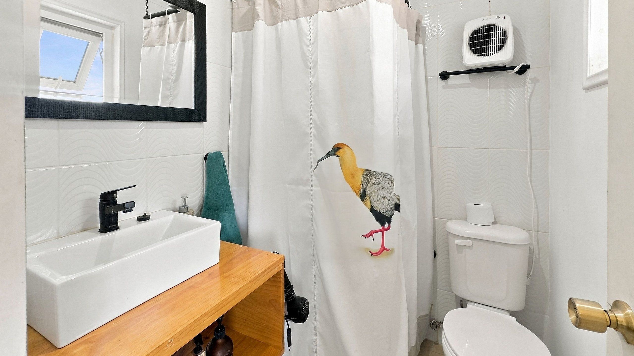 Un baño con lavamanos blanco, un espejo, inodoro y cortina de ducha con diseño de pájaros.