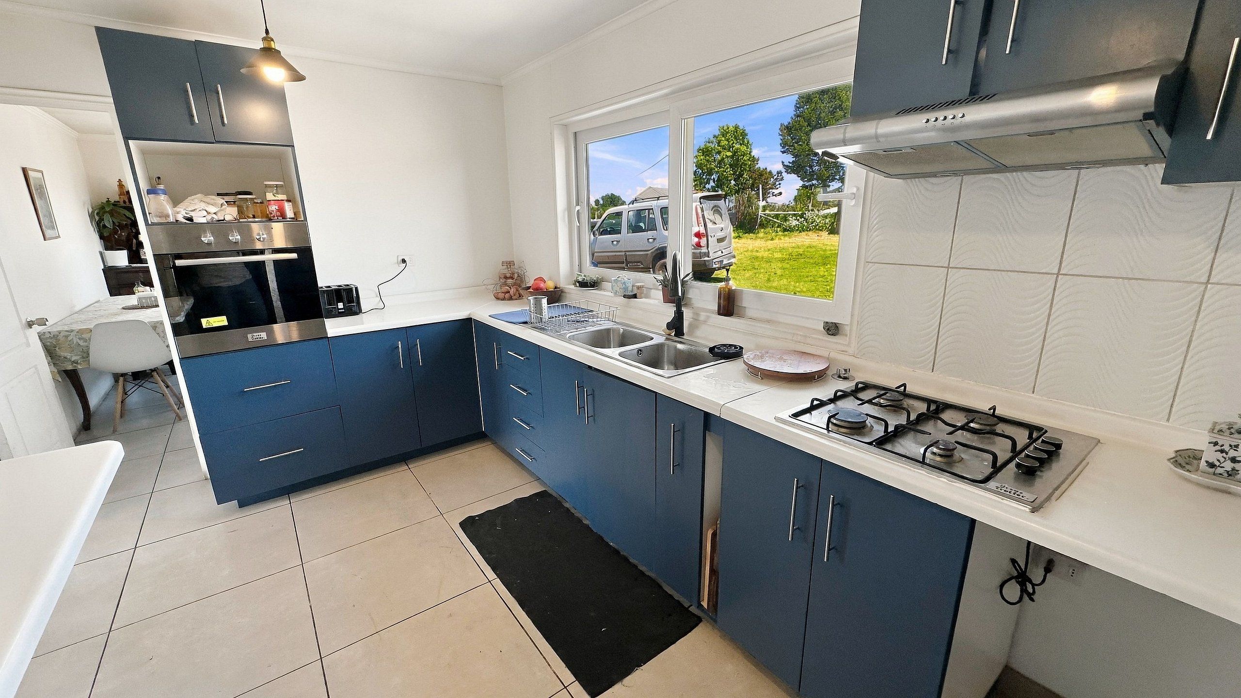 Una cocina moderna con armarios azules, una estufa a gas, un lavamanos y un ventanal con vistas a un paisaje verde.