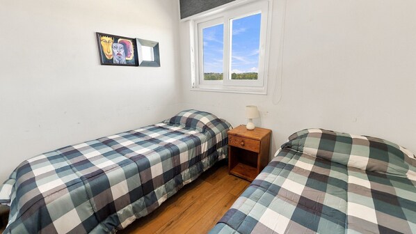 Una habitación con dos camas, una ventana, una mesita de noche y un cuadro colgado en la pared.