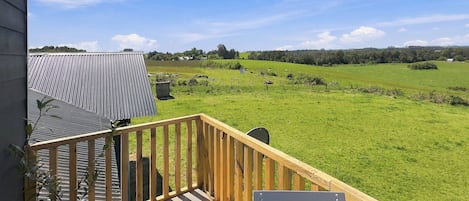 A wooden deck with a view of a green field and distant hills.