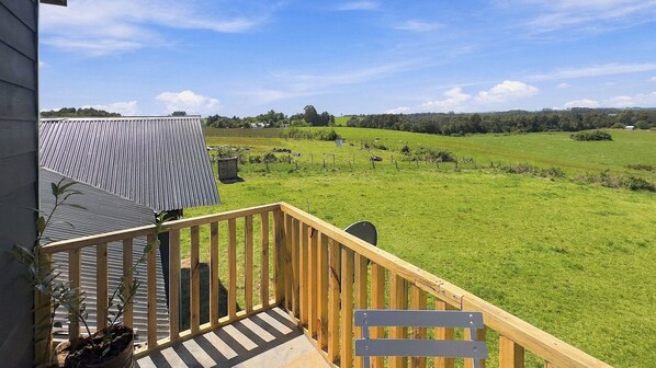 A wooden deck with a view of a green field and distant hills.