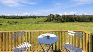 A wooden deck with a table and two chairs, overlooking a green field and trees. - Oceana Suites Sueño Rural (Puerto Varas)