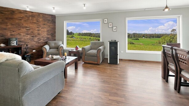 A spacious living room with a large window, a fireplace, and a view of a green landscape. - Oceana Suites Sueño Rural (Puerto Varas)