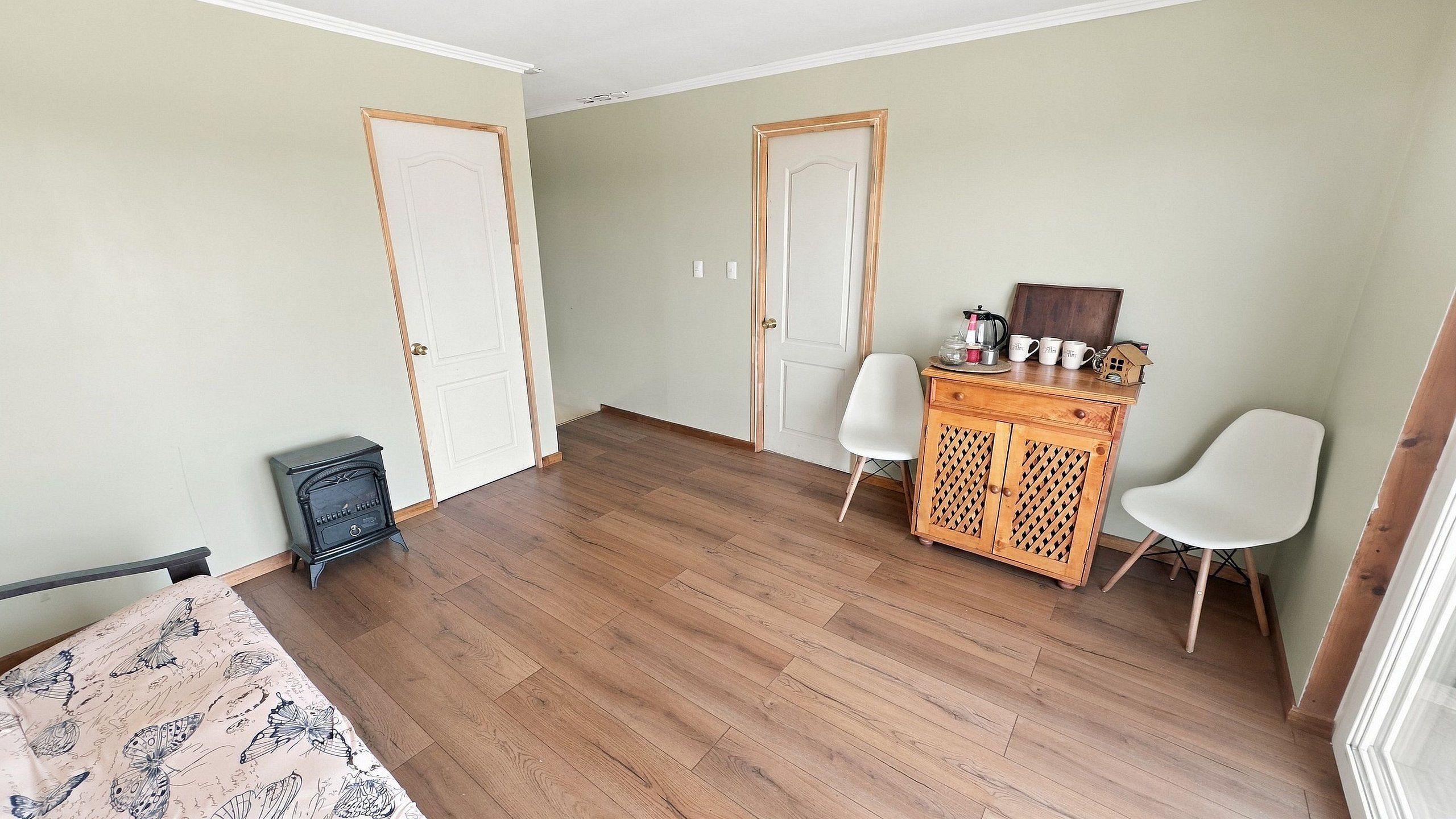 Een kamer met houten vloer, twee witte deuren, een klein kastje met lades en een witte stoel.