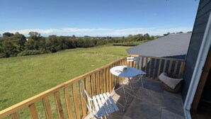 A balcony with a table and chairs, overlooking a grassy field and trees. - Oceana Suites Sueño Rural (Puerto Varas)