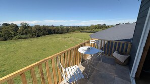 A balcony with a table and chairs, overlooking a grassy field and trees.
