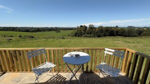 Una terraza de madera con una mesa y dos sillas, con vistas a un campo verde y árboles.