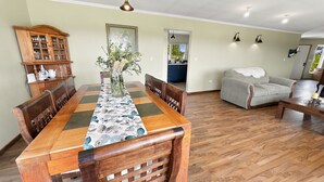 A dining area with a wooden table, chairs, a vase with flowers, and a kitchen visible through an open doorway. - Oceana Suites Sueño Rural (Puerto Varas)