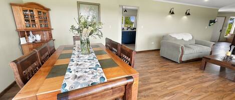 A dining area with a wooden table, chairs, a vase with flowers, and a kitchen visible through an open doorway.