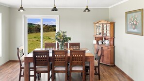 A dining area with a table and chairs, a cabinet with glass doors, and a view of a green landscape through a door.