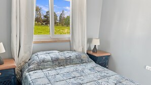 A bedroom with a bed, a window with curtains, a bedside table with a lamp, and a nightstand with a lamp. - Oceana Suites Sueño Rural (Puerto Varas)