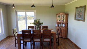 Comedor con mesa de madera, cuatro sillas, un jarrón con flores, una vitrina con puertas de cristal y un cuadro en la pared.