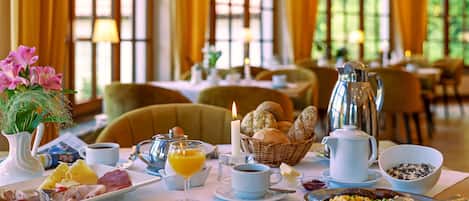 A breakfast setting with a variety of food items, including eggs, bread, and pastries, arranged on a table in a well-lit room with large windows.