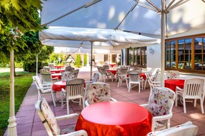 An outdoor patio with white chairs and tables, covered by large umbrellas, and surrounded by greenery. - Hotel Mügge am Iberg (Oerlinghausen)