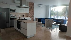 Una cocina moderna con una isla central, armarios blancos y una pared de acento de piedra. Hay una zona de comedor con un sofá azul y una mesa pequeña.