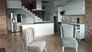 A modern kitchen with a central island, stainless steel appliances, and a staircase leading to an upper level. - RESORT FRENTE AL MAR (Juan de Acosta)