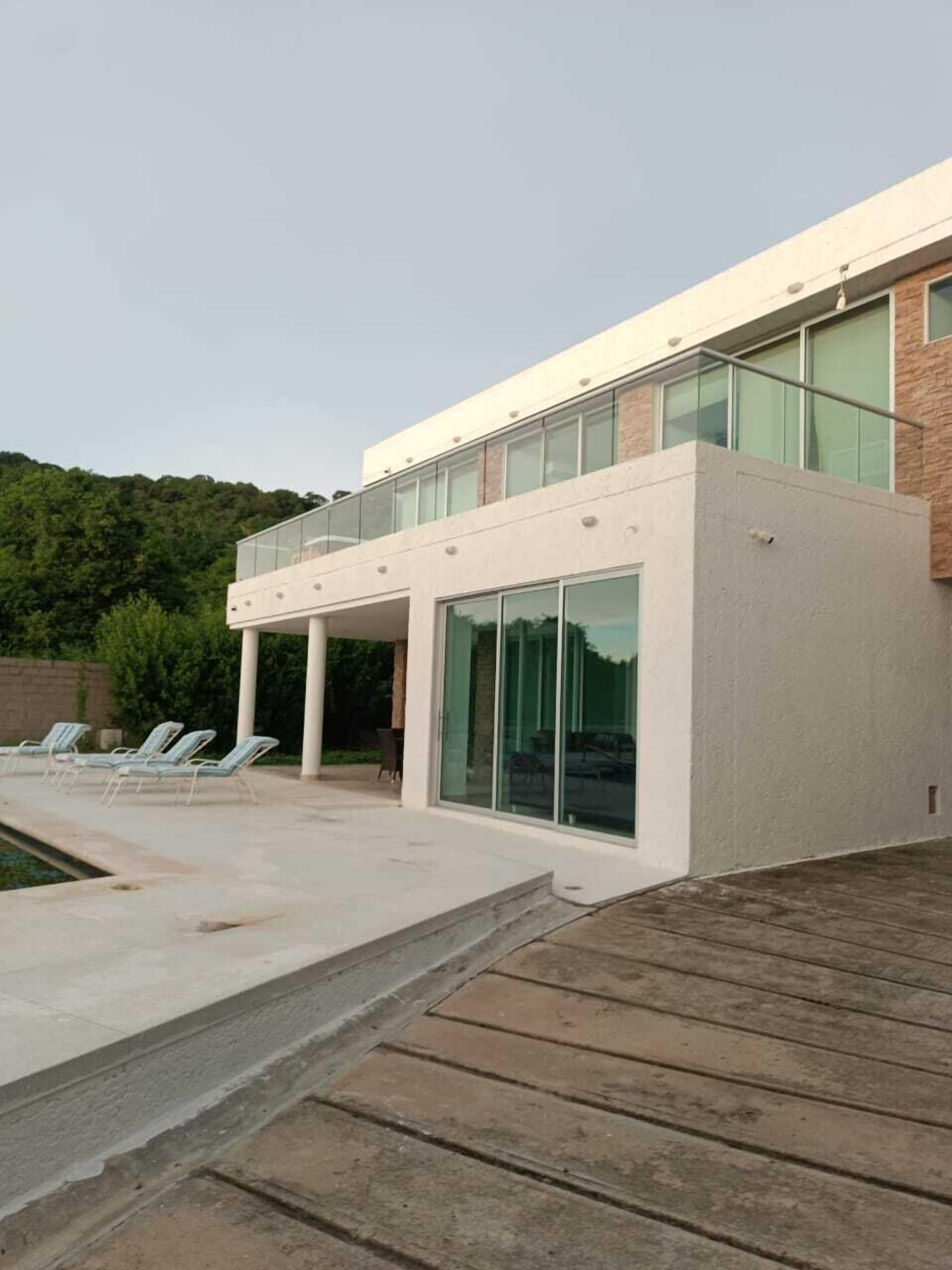 Un edificio moderno con fachada de vidrio, un área de piscina con sillones reclinables y una terraza de madera.