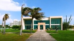 Un edificio moderno con una entrada central, rodeado por un césped cuidado y palmeras.