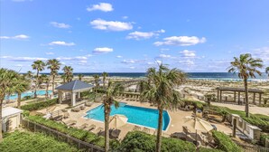 A resort with a swimming pool, palm trees, and a beach view. - Beach Club 1109 D (Gulf Shores)