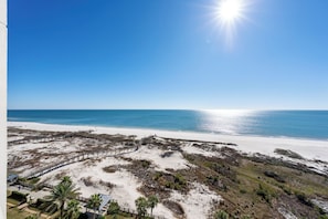 Una playa con un paseo marítimo de madera, dunas arenosas y un cielo azul despejado.