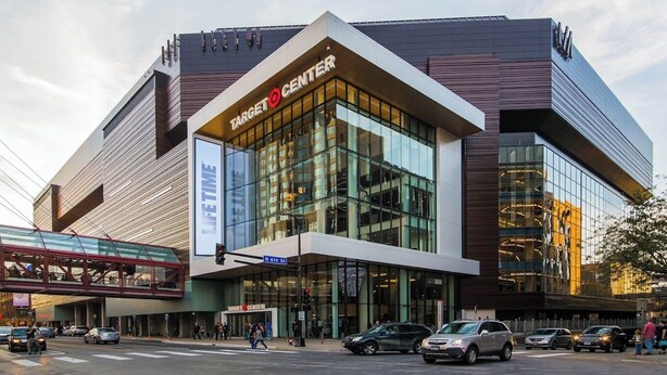 Um edifício moderno do Target Center com fachada de vidro, uma passarela e vista da rua com carros e pedestres.