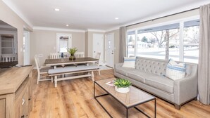 Uma sala de estar moderna com piso de madeira, um sofá, uma mesa de centro e um espaço de jantar com mesa e cadeiras.