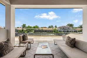 A balcony with a sofa, armchairs, and a coffee table, overlooking a modern building and palm trees.