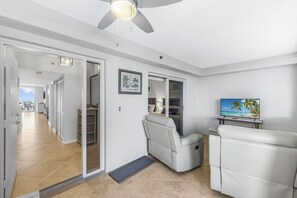 A modern living room with a ceiling fan, a TV, and a sliding door leading to a balcony. - The Somerset Solace | Pools, Tennis Courts & Gym (Marco Island)