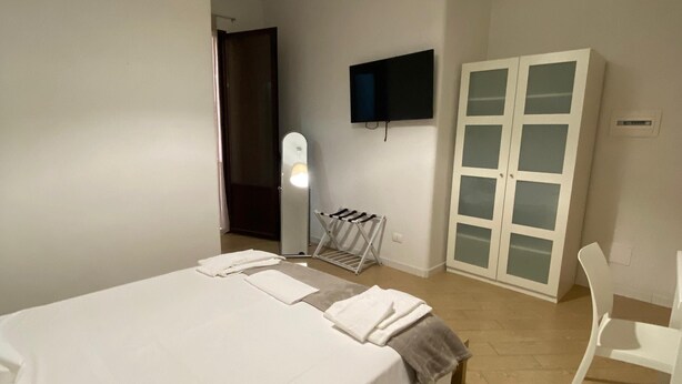 A bedroom with a bed, a TV mounted on the wall, a wardrobe, and a chair. - Manu's house B&B (Porto Empedocle)