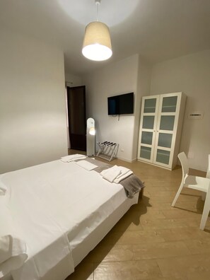 Un dormitorio con cama, televisor montado en la pared, armario y una silla.
