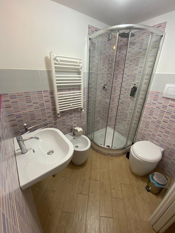 A bathroom with a sink, bidet, toilet, and glass shower enclosure. - Manu's house B&B (Porto Empedocle)