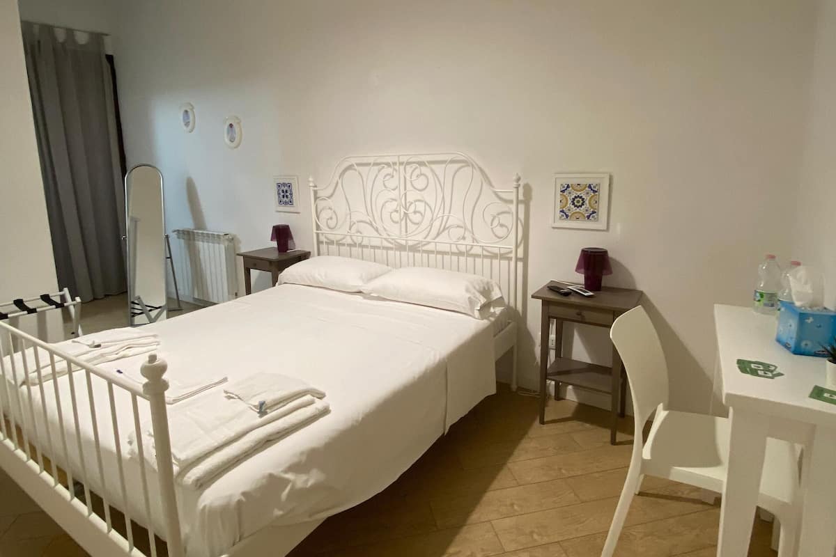 A neatly arranged bedroom with a bed, bedside table, chair, and a hanging light fixture.
