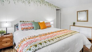 Een keurig opgemaakt slaapkamer met een bed, nachtkastjes, een plafondventilator en een spiegel aan de muur.