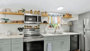 Een moderne keuken met grijze kastjes, roestvrijstalen apparatuur en decoratieve, huisvormige objecten op planken.