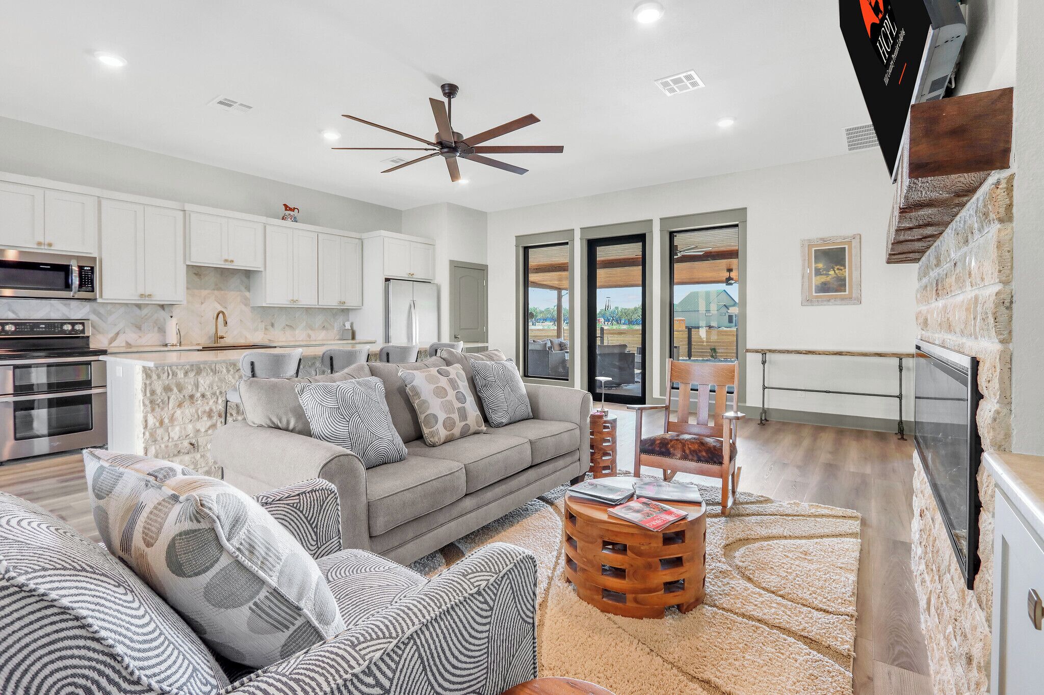 A modern kitchen with white cabinets, a microwave, and a stove. There is a gray sofa with patterned cushions and a wooden coffee table.