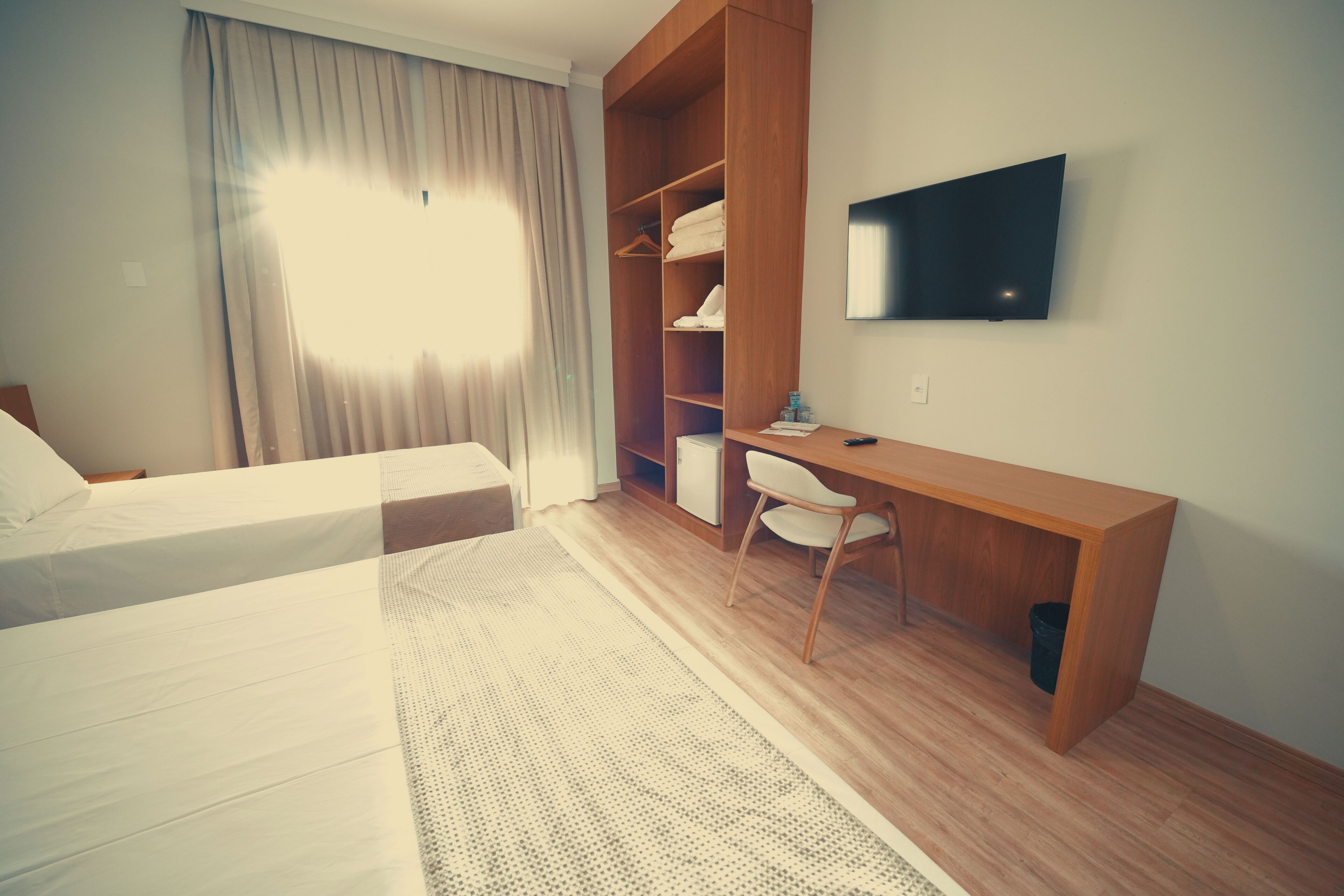 Habitación de hotel con cama, escritorio, silla, televisor y armario.