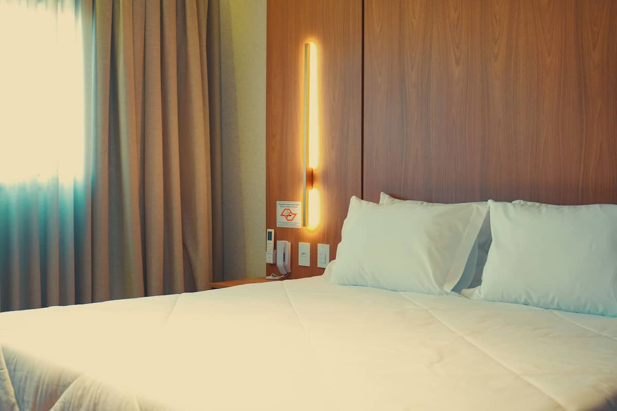 Une chambre d’hôtel avec un lit, une table de chevet avec un téléphone et une lampe fixée au mur.
