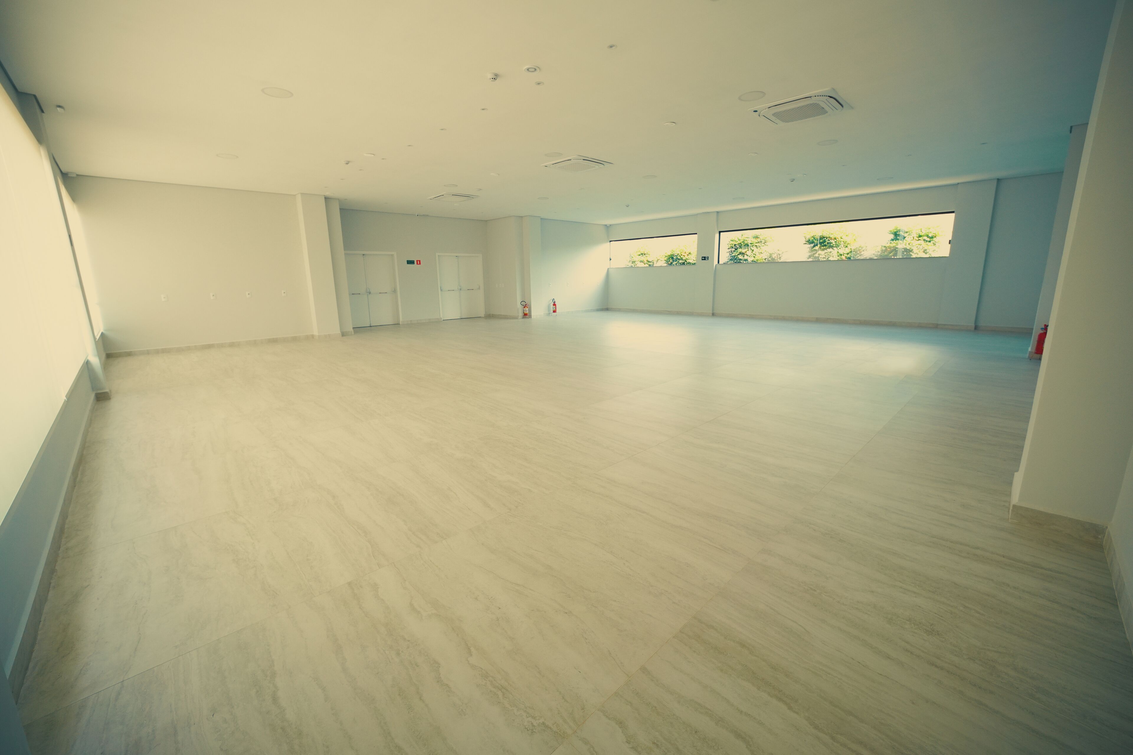 A spacious room with a light-colored floor, white walls, and a large window allowing natural light.