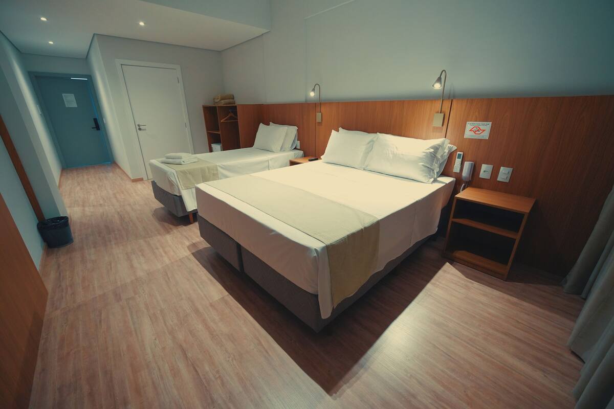 Une chambre d’hôtel avec deux lits, une tête de lit en bois, des tables de chevet et une commode, ainsi qu’une porte.