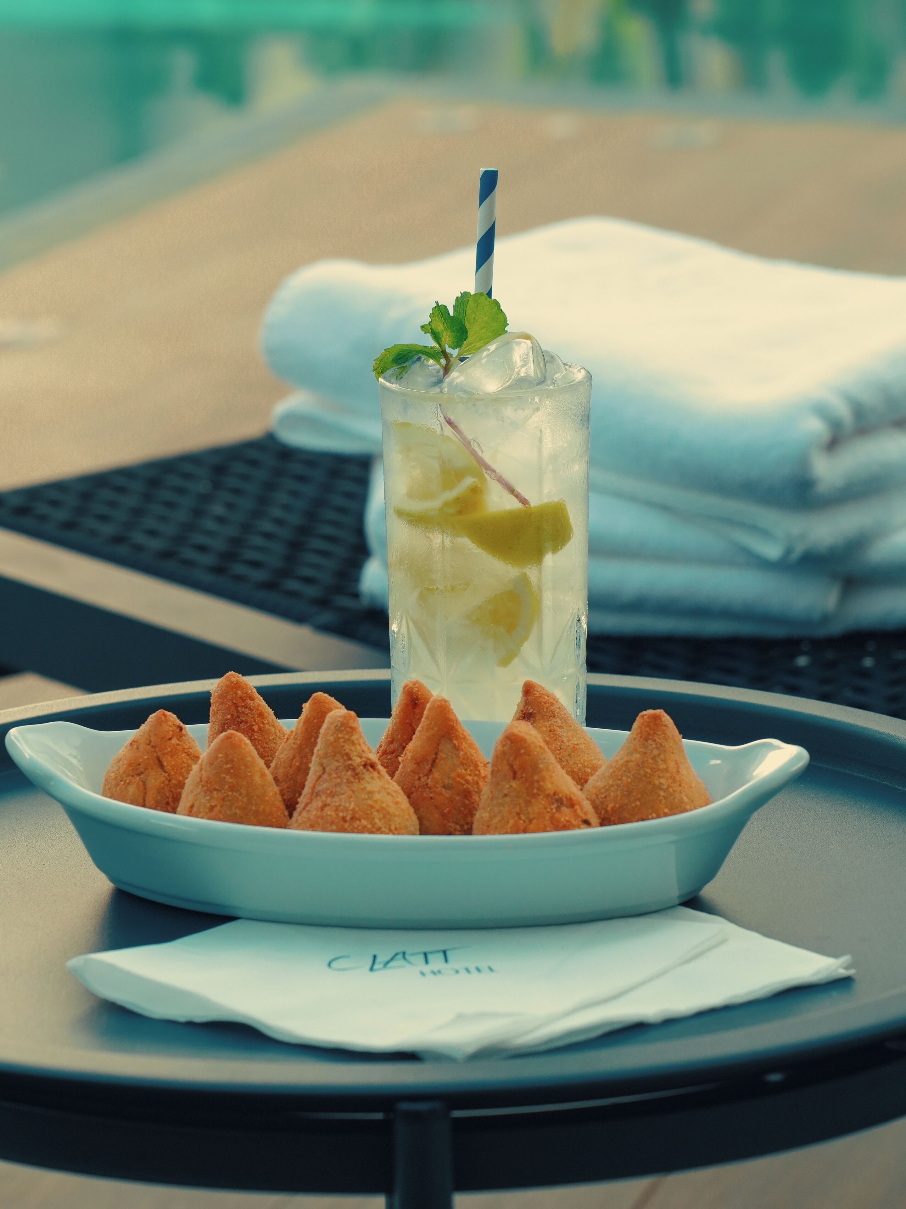 Un bicchiere di bevanda fredda con una cannuccia e una fetta di lime, un piatto di stuzzichini fritti e un tovagliolo su un tavolo.