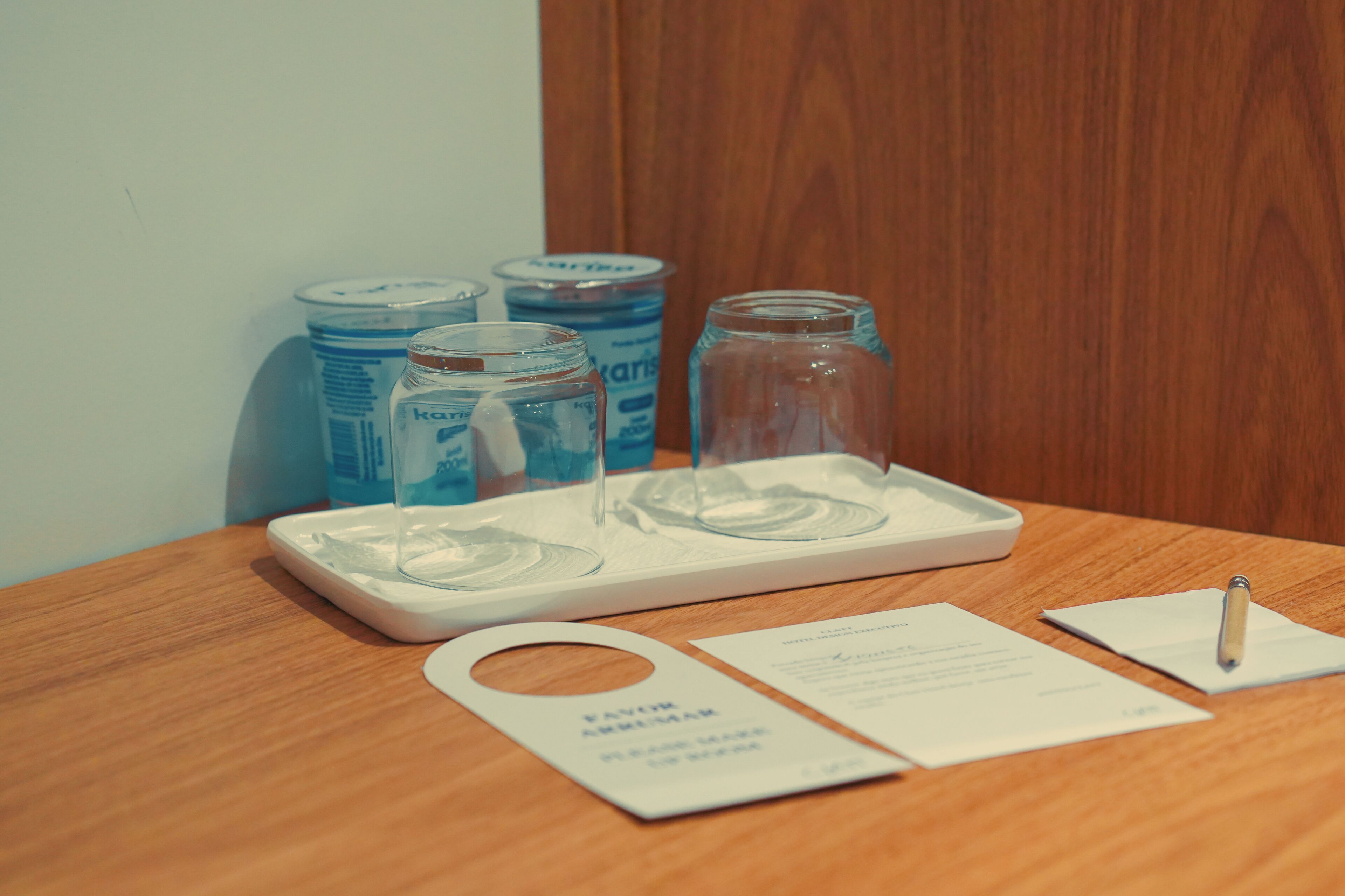 A wooden table with a tray holding two clear glasses, a pen, and a card.